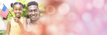 Portrait of happy father and daughter holding American flags on sunny day at parkの写真素材