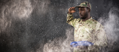 Portrait of soldier holding American flag and saluting against blackの写真素材