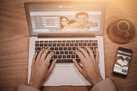 Dating site against businesswoman using laptop with coffee and mobile phone on deskの写真素材