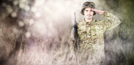 Portrait of soldier holding rifle and saluting against dark backgroundの写真素材