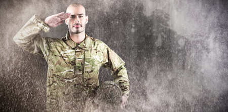 Portrait of confident soldier holding helmet while saluting  against blackの写真素材