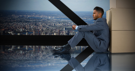 Businessman leaning on cardboard boxes against white background against room with large window looking on cityの写真素材