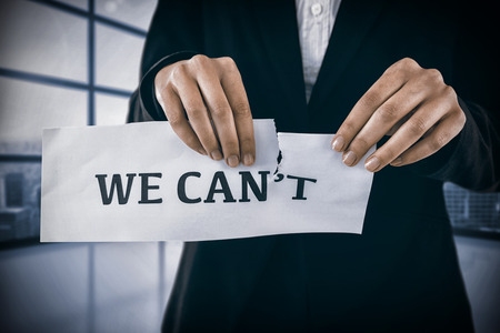 Conceptual image of businesswoman tearing a paper that reads we cant against room with large window showing cityの写真素材