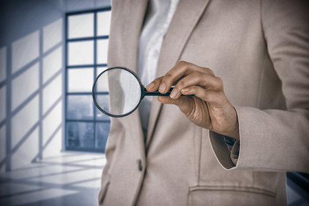 Mid section of businesswoman holding magnifying glass against room with large window showing cityの写真素材