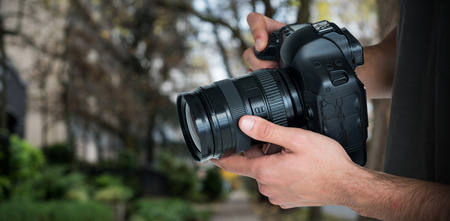 Mid section of male photographer holding camera  against footpath by trees in city