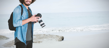 Portrait of smiling male photographer holding camera  against beachの写真素材