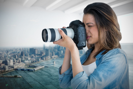Young female photographer photographing through camera against city scene in a roomの写真素材