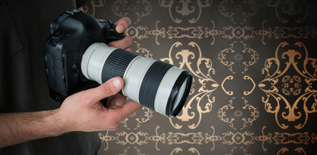 Mid section of male photographer holding digital camera against room with ornate wallpaper
