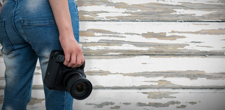 Mid section of woman holding digital camera against wood plank with grey paintの写真素材