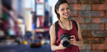 Portrait of happy female photographer with digital camera against wall of a house
