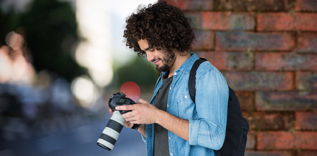 Young male photographer operating camera  against wall of a house