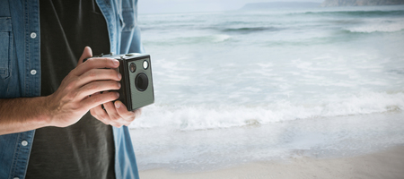 Mid section of photographer holding vintage camera  against sea against sky