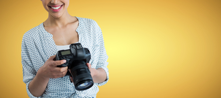 Portrait of smiling young woman holding digital camera against yellow vignetteの写真素材