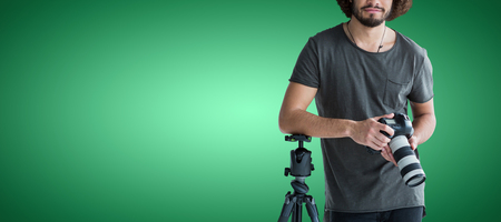 Portrait of young photographer holding digital camera against green vignette