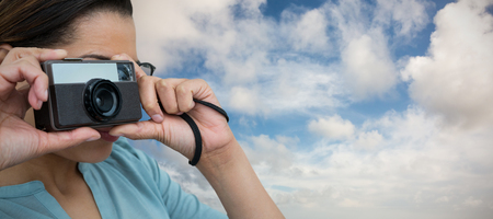 Close up of woman photographing with camera against blue sky with white cloudsの写真素材