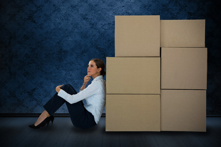 Businesswoman leaning on cardboard boxes against white background against dark grimy roomの写真素材