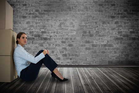 Businesswoman leaning on cardboard boxes against white background against grey room with parquet floorの写真素材