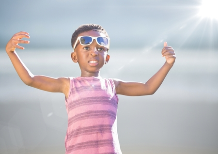 Digital composite of Boy in sunglasses hands out against blurry beach with flare