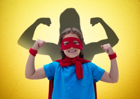 Digital composite of happy girl dressing up like a superwoman in front of fists draw on yellow wallの写真素材