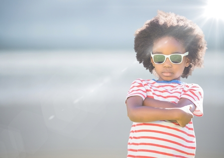 Digital composite of Boy in sunglasses arms folded against blurry beach with flareの写真素材