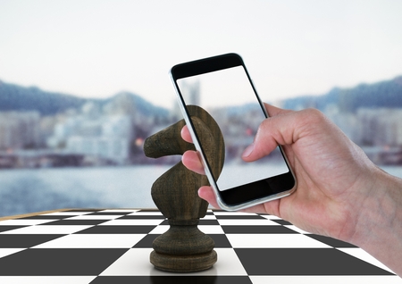 Digital composite of Hand with device against 3D chess piece and blurry skylineの写真素材