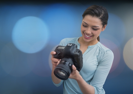 Digital composite of photographer smiling looking the photos on the camera. Blue blurred lights on backの写真素材