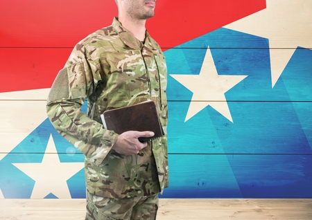 Digital composite of Side view of soldier holding a book in front of american flag