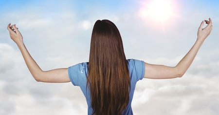 Digital composite of Back of woman with arms outstretched against sunny skyの写真素材