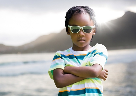 Digital composite of Boy in sunglasses arms folded against coastline with flareの写真素材