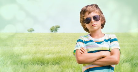 Digital composite of Boy with sunglasses arms folded against meadowの写真素材