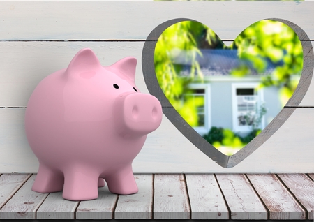 Digital composite of pink piggy bank in front of wood wall with heart hole where we can see a house (blurred)の写真素材