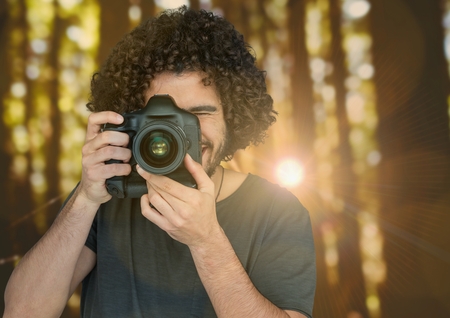 Digital composite of photographer taking a photo on forest with flare behind and blurred lights...