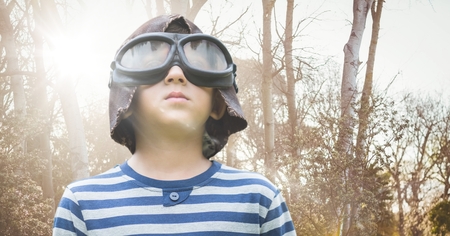 Digital composite of Boy with goggles against blurry trees with flare