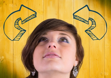 Digital composite of Woman looking up at blue curved 3D arrows against yellow wood panelの写真素材