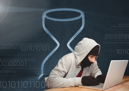 Digital composite of 3D Hacker using a laptop in front of digital background with an hourglass