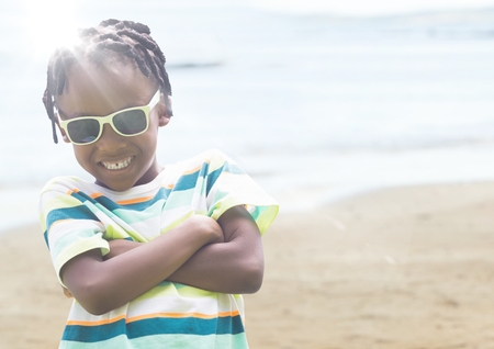 Digital composite of Boy in sunglasses arms folded against blurry beach with flareの写真素材