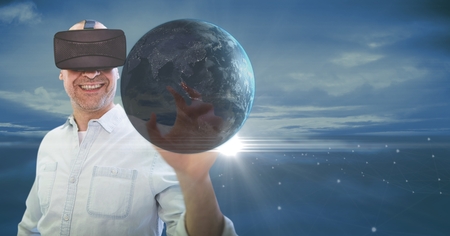 Digital composite of Happy man in VR touching 3D planet with flares against blue sky