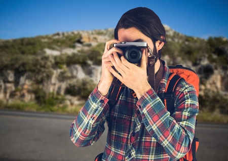 Digital composite of Millennial backpacker with camera against road and rock