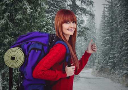 Digital composite of Millennial backpacker thumbs up against snowy forestの写真素材