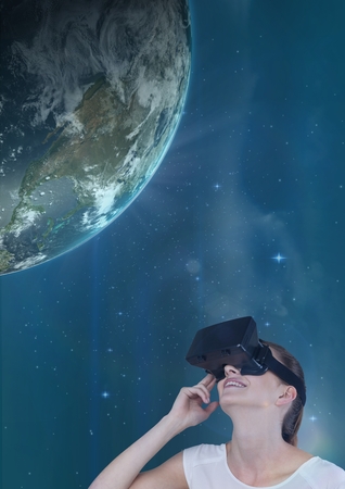 Digital composite of Woman in VR headset looking up to a 3D planet against blue sky