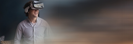 Digital composite of Man laughing in virtual reality headset against grey wall and blurry sunset transition and copy spaceの写真素材