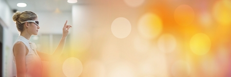 Digital composite of Woman pointing in white virtual reality headset and orange bokeh transition 3d