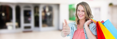 Digital composite of Shopper with bags giving thumbs up against blurry  shopping centreの写真素材