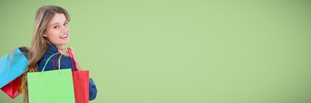 Digital composite of Shopper with bags looking over shoulder against green backgroundの写真素材