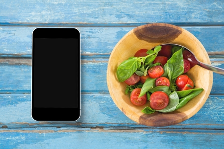 Digital composite of Phone on blue wooden desk with food and copy space on mobile phoneの写真素材