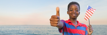 Digital composite of Boy with american flag giving thumbs up against water and evening skyの写真素材