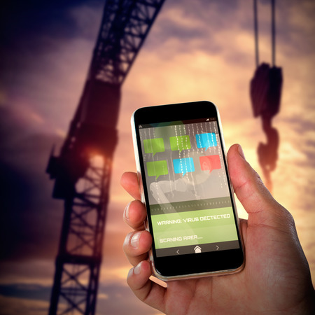 Close-up of hand holding mobile against low angle 3d image of silhouette crane