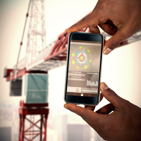 Close up of hand holding mobile phone against 3d effect of red and white craneの写真素材