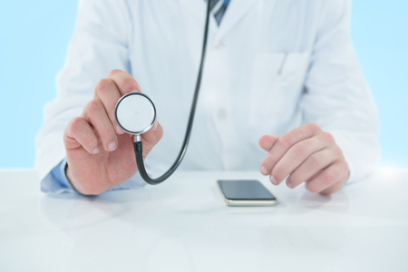 Midsection of doctor holding stethoscope against 3D blue vignette backgroundの写真素材