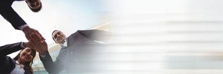 Digital composite of Low angle of business team putting hands together and blurry white transitionの写真素材
